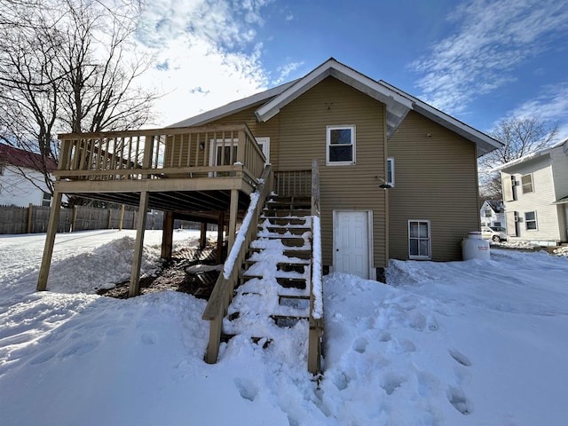 snow covered rear of property with fence, stairway, and a wooden deck