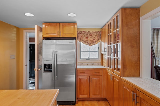 kitchen featuring glass insert cabinets, stainless steel fridge, tile countertops, and light wood finished floors