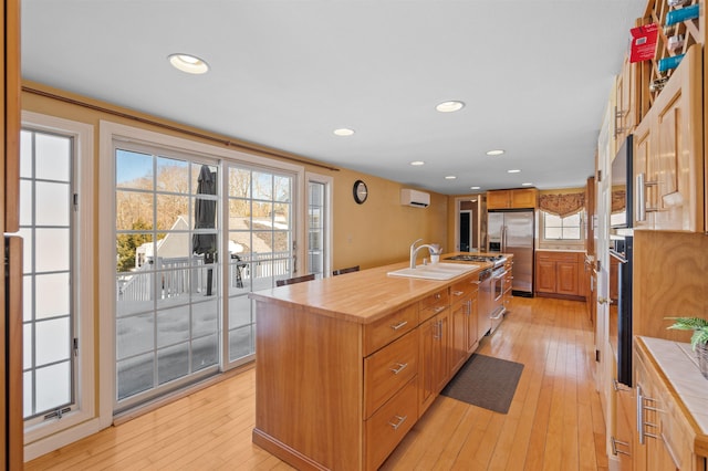 kitchen with a wall unit AC, a kitchen island with sink, stainless steel refrigerator with ice dispenser, wooden counters, and a sink