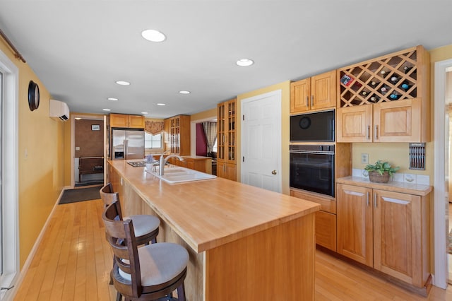 kitchen featuring a center island with sink, light countertops, a sink, stainless steel fridge, and a kitchen breakfast bar