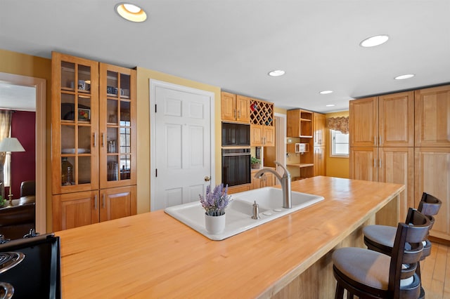 kitchen featuring butcher block counters, glass insert cabinets, a kitchen breakfast bar, a sink, and recessed lighting