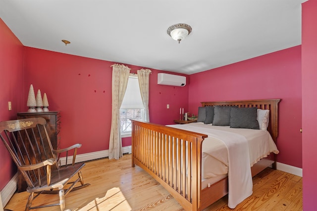 bedroom with a baseboard heating unit, a wall unit AC, wood finished floors, and baseboards