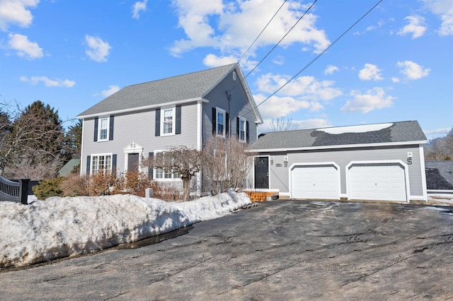 colonial inspired home with a garage, aphalt driveway, and roof with shingles