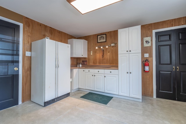 kitchen with wood walls, concrete floors, white cabinetry, and freestanding refrigerator