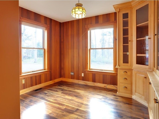 unfurnished room with a healthy amount of sunlight, wood walls, and visible vents