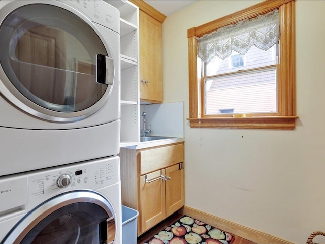 washroom with stacked washer / drying machine, cabinet space, a sink, and baseboards