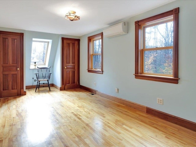 empty room with plenty of natural light, light wood finished floors, and a wall unit AC