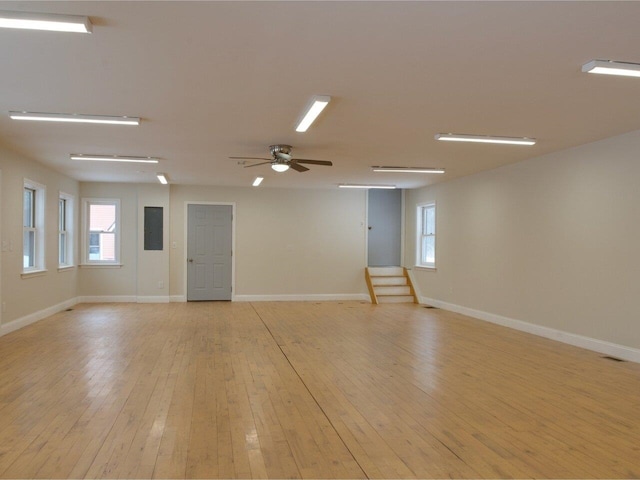 spare room featuring a wealth of natural light, light wood-style flooring, a ceiling fan, baseboards, and stairs