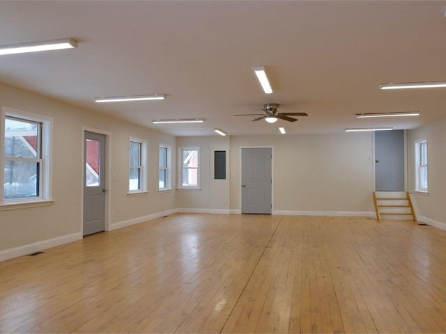 spare room featuring stairway, a wealth of natural light, light wood-style flooring, and baseboards