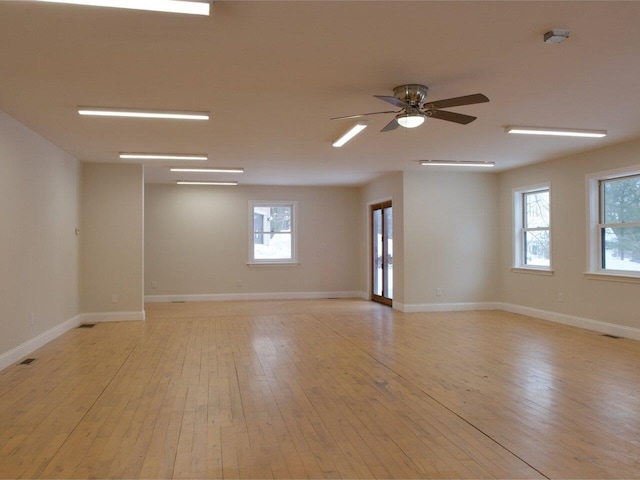 unfurnished room featuring a ceiling fan, a wealth of natural light, light wood-style flooring, and baseboards