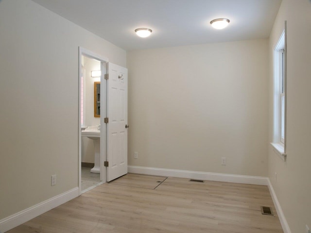 unfurnished bedroom featuring light wood-style floors, baseboards, visible vents, and ensuite bathroom