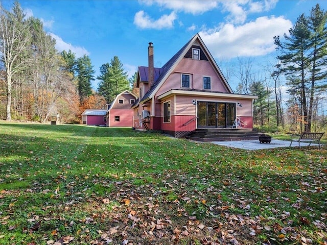 back of house featuring entry steps, an outdoor fire pit, a patio, a chimney, and a yard