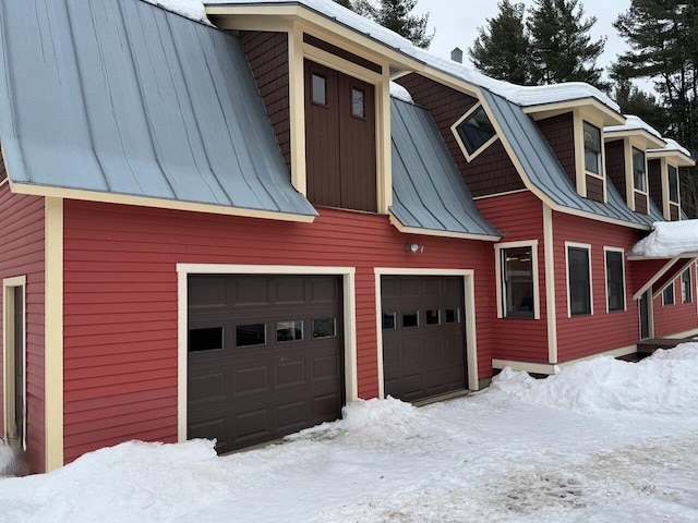 snow covered property featuring a garage, metal roof, a standing seam roof, and a barn