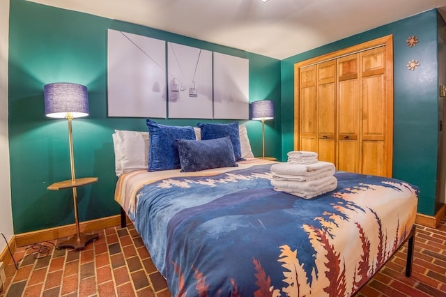 bedroom featuring brick floor, a closet, and baseboards