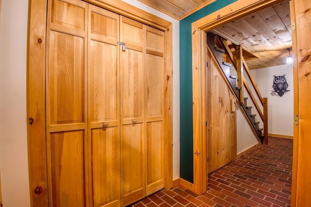 hallway featuring brick floor, baseboards, and stairway