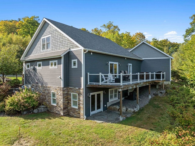 back of property featuring a shingled roof, a deck, and a lawn