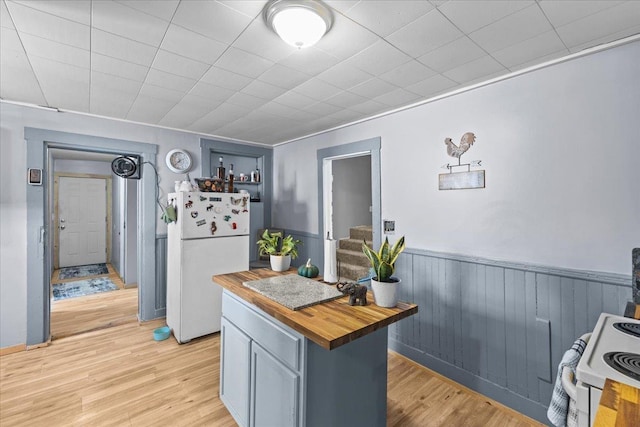 kitchen featuring white appliances, butcher block countertops, light wood finished floors, and wainscoting