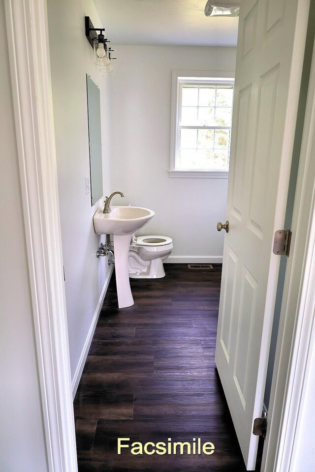 half bath featuring visible vents, toilet, a sink, wood finished floors, and baseboards