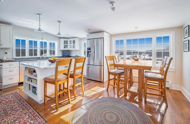 kitchen with stainless steel refrigerator with ice dispenser, light wood finished floors, open shelves, white cabinets, and a kitchen bar