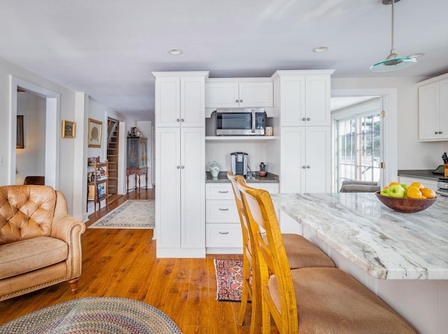 kitchen featuring light wood finished floors, white cabinets, built in study area, stainless steel microwave, and recessed lighting