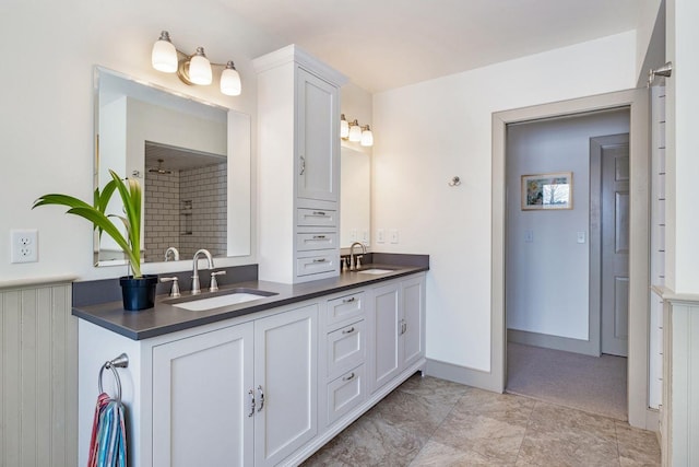 full bathroom featuring double vanity, baseboards, a tile shower, and a sink