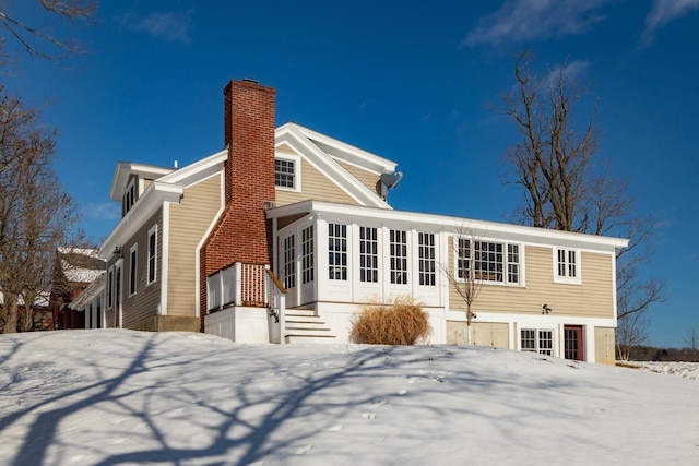 snow covered back of property with a chimney and a sunroom