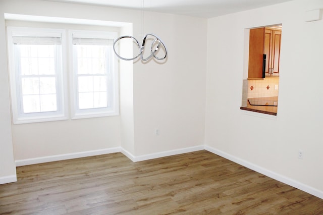 spare room with light wood-type flooring, baseboards, and a chandelier