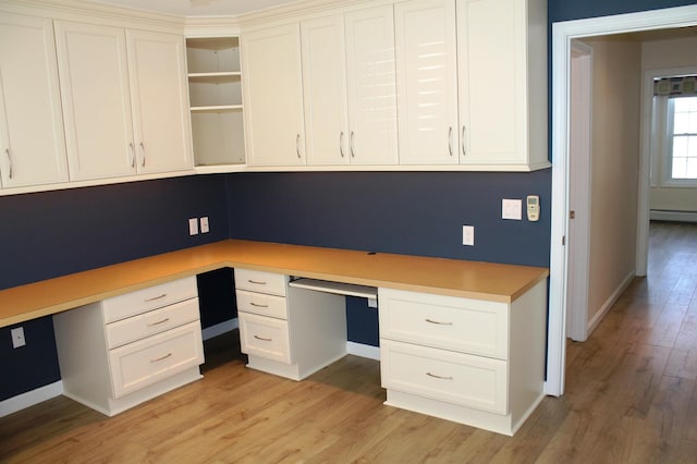 unfurnished office featuring light wood-type flooring, built in desk, and baseboards