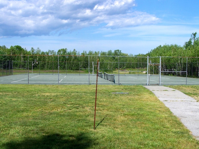 view of tennis court with a lawn and fence