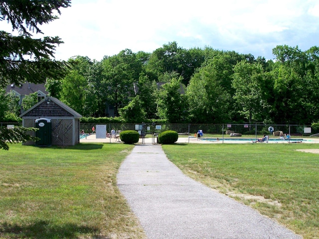 view of community with fence, a pool, and a yard