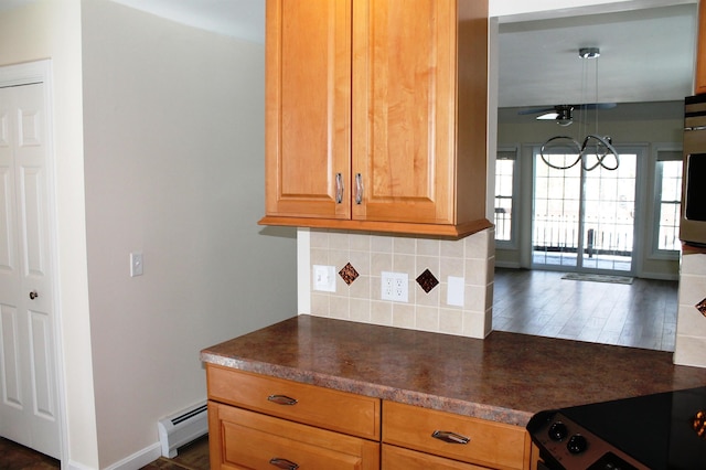 kitchen featuring baseboards, baseboard heating, backsplash, dark wood-style floors, and dark countertops