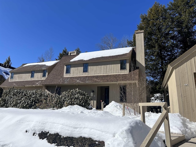 view of snowy exterior with a shingled roof and a chimney