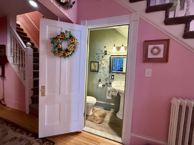 half bathroom featuring radiator, baseboards, toilet, and wood finished floors