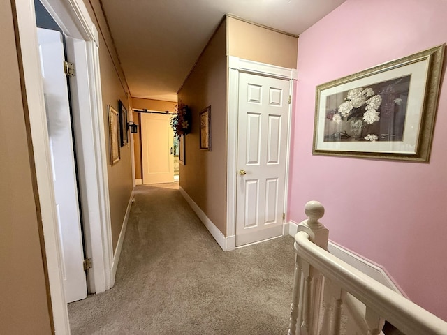 corridor with an upstairs landing, carpet flooring, baseboards, and a barn door