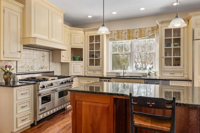 kitchen with range with two ovens, custom range hood, glass insert cabinets, dark stone countertops, and a sink