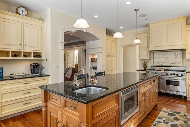 kitchen featuring arched walkways, stainless steel appliances, cream cabinets, and a sink