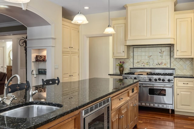 kitchen featuring arched walkways, cream cabinets, appliances with stainless steel finishes, dark wood-type flooring, and a sink