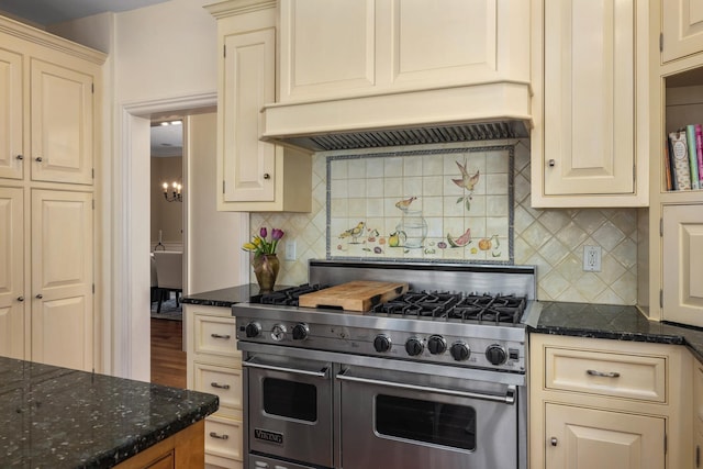 kitchen featuring range with two ovens, cream cabinetry, custom exhaust hood, decorative backsplash, and dark stone countertops