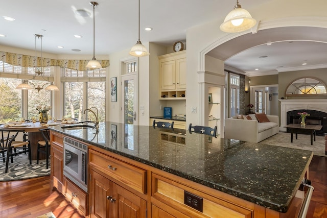 kitchen featuring arched walkways, a fireplace, wood finished floors, a sink, and stainless steel microwave