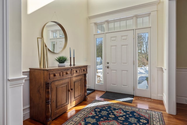 foyer entrance with light wood-style floors, visible vents, and wainscoting