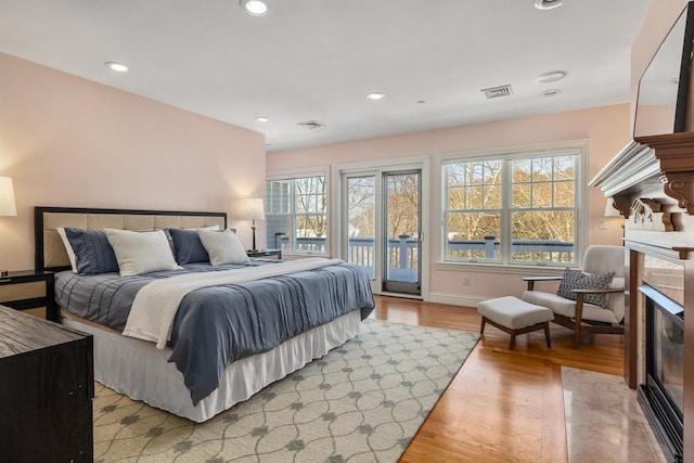 bedroom featuring access to exterior, recessed lighting, visible vents, light wood-style floors, and a glass covered fireplace