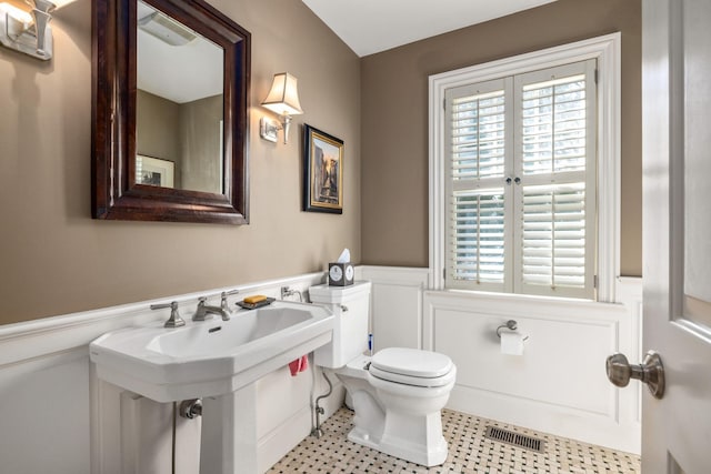 half bath with visible vents, wainscoting, toilet, and a decorative wall