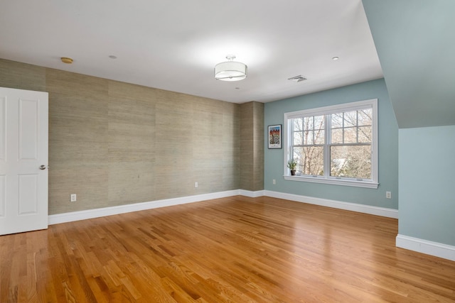 spare room with light wood finished floors, wallpapered walls, visible vents, baseboards, and an accent wall