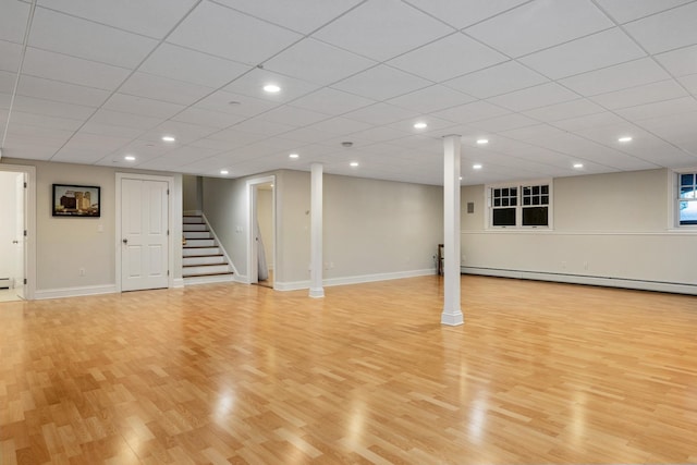 finished basement featuring a baseboard heating unit, light wood-style floors, stairway, and baseboards