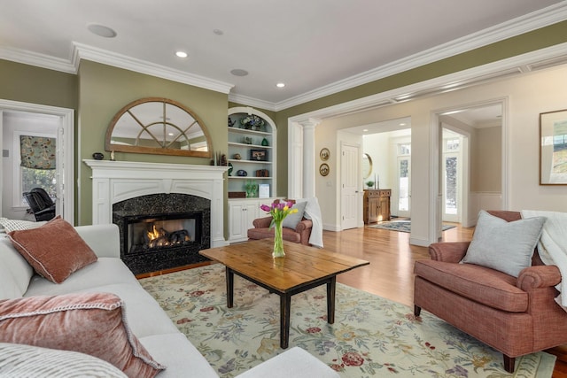 living area with built in shelves, decorative columns, ornamental molding, a high end fireplace, and wood finished floors