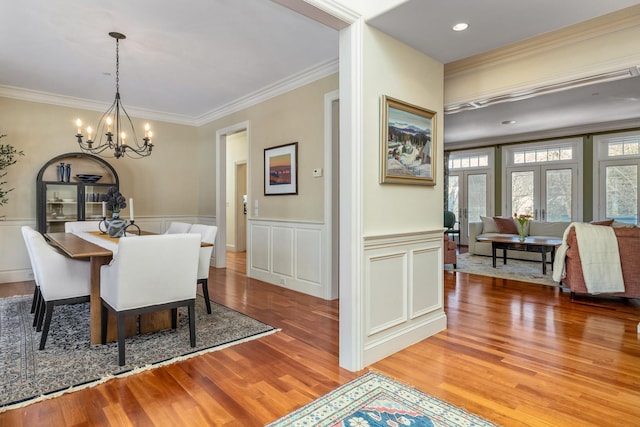 dining space with an inviting chandelier, french doors, crown molding, and wood finished floors