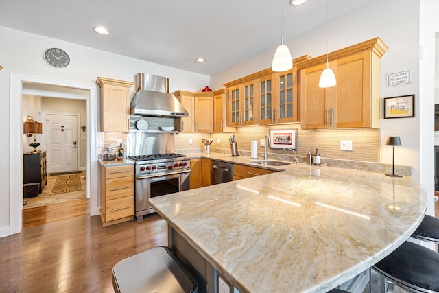 kitchen featuring a peninsula, stainless steel appliances, a sink, a kitchen breakfast bar, and wall chimney exhaust hood