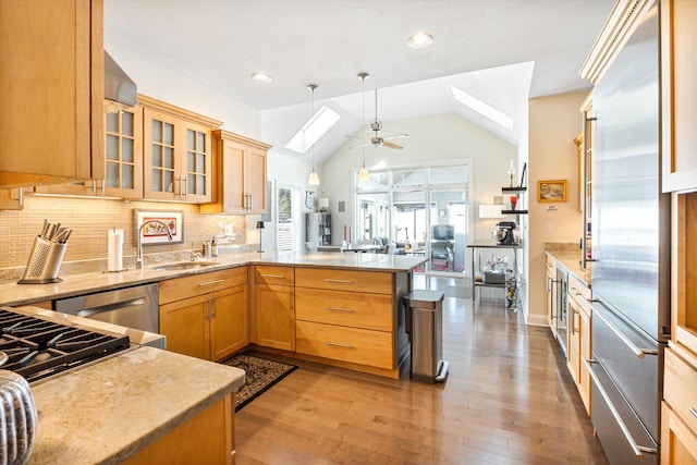 kitchen featuring tasteful backsplash, appliances with stainless steel finishes, a peninsula, light wood-type flooring, and a sink