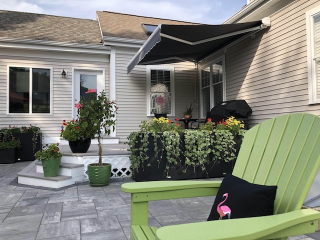 view of exterior entry featuring roof with shingles and a patio