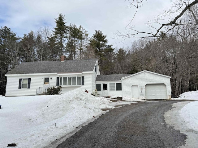 view of front facade featuring a shingled roof, driveway, a chimney, and an attached garage